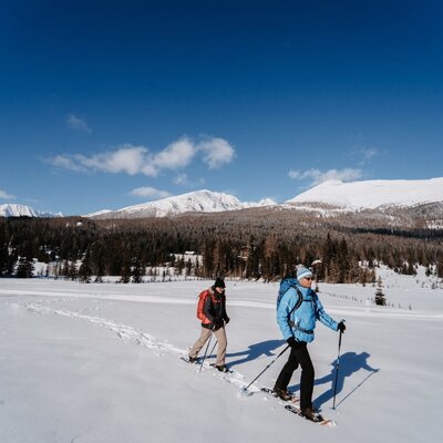 Two people snowshoeing in the winter landscape surrounding the farmhouse.