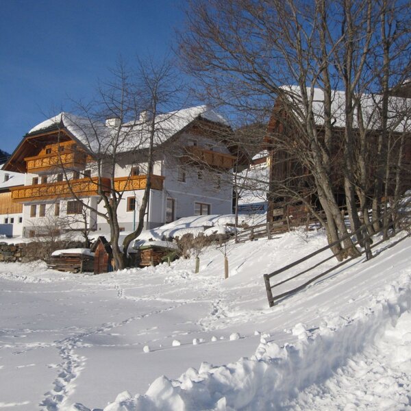 The farmhouse exterior, featuring wooden balconies and an adjacent wooden barn, is visible in a snow-covered setting.