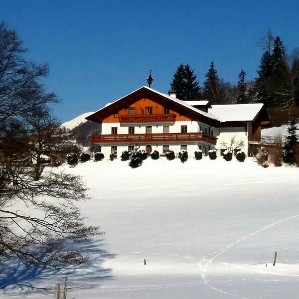 The Farm House exterior with traditional wooden balconies, set amidst snow-covered fields and trees.
