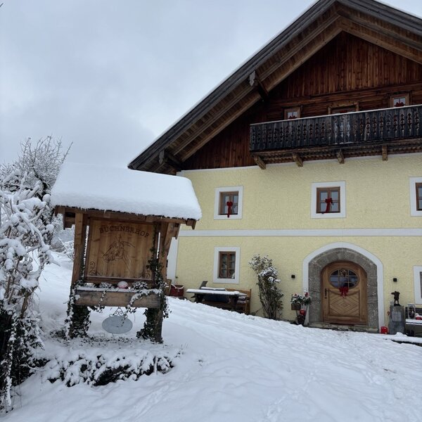 The snow-covered farmhouse with a wooden balcony and a traditional entrance in winter.