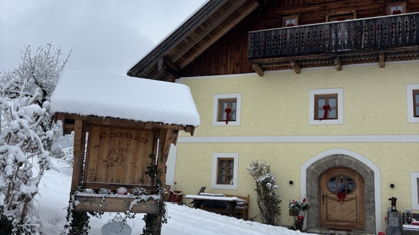 The snow-covered farmhouse with a wooden balcony and a traditional entrance in winter.