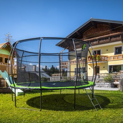 The farmhouse's inviting play area featuring a large trampoline, a wooden playhouse, and a slide on a sunny lawn.
