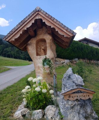 A beautifully crafted wooden shrine and stone welcome sign surrounded by lush hydrangeas at the farmhouse.