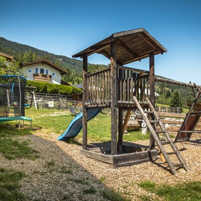 The farmhouse's inviting playground featuring a wooden climbing tower, a slide, swings, and a trampoline.