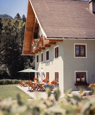 The exterior of the Farm House, featuring a balcony with red flower boxes and an outdoor patio with wooden seating and a parasol.