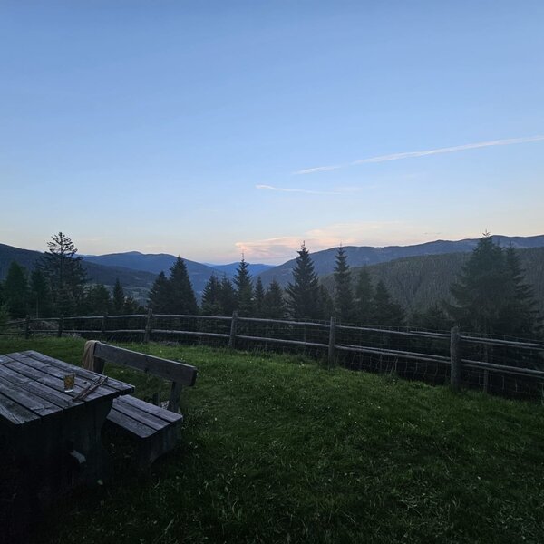 Outdoor area of the Bed and Breakfast with a wooden table, benches, and a view of the mountains and forests.