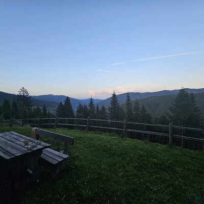 Outdoor area of the Bed and Breakfast with a wooden table, benches, and a view of the mountains and forests.