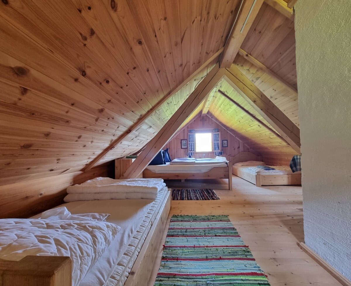 Attic bedroom of the Almhütte with multiple beds, wooden walls, and a window.