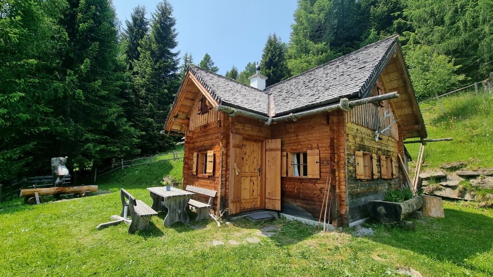 The almhut exterior, surrounded by forest and meadows, featuring an outdoor dining area.