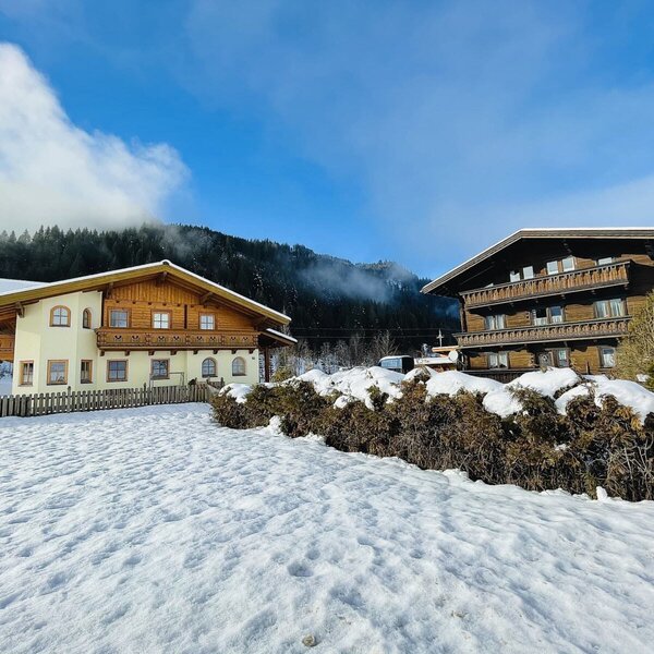 The exterior of the farm house, featuring traditional buildings with wooden balconies, surrounded by a snowy mountain landscape.