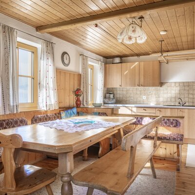 The farmhouse kitchen-diner features a wooden dining table with built-in corner benches and chairs, complemented by a kitchen area with wooden cabinets, a sink, and a wood-burning stove.