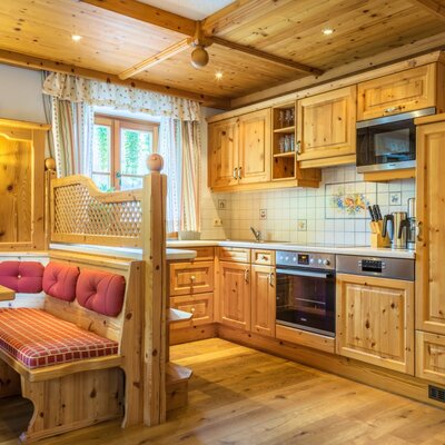 The holiday apartment's kitchen/living room in the Farm House offers a fully equipped kitchen with a microwave, oven, dishwasher, and fridge, alongside a dining area with a wooden corner bench.