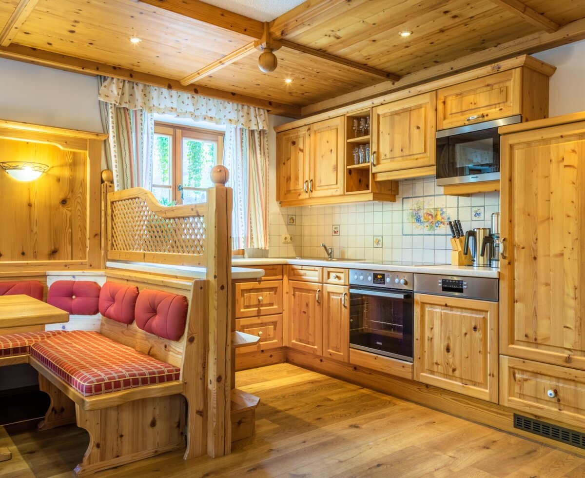 The holiday apartment's kitchen/living room in the Farm House offers a fully equipped kitchen with a microwave, oven, dishwasher, and fridge, alongside a dining area with a wooden corner bench.