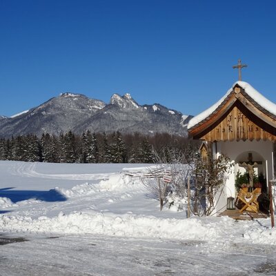 A snow-covered wayside shrine with mountain views in the winter landscape surrounding the farm house.