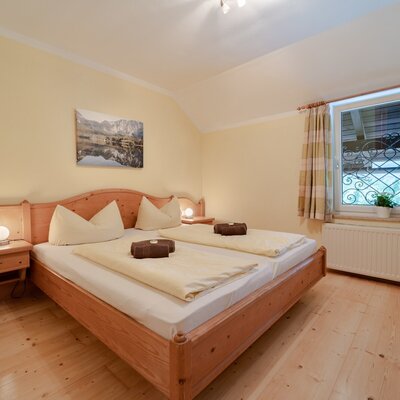 Double bedroom in the Farm House with a wooden double bed, two bedside tables with lamps, and a window with a decorative security grill.