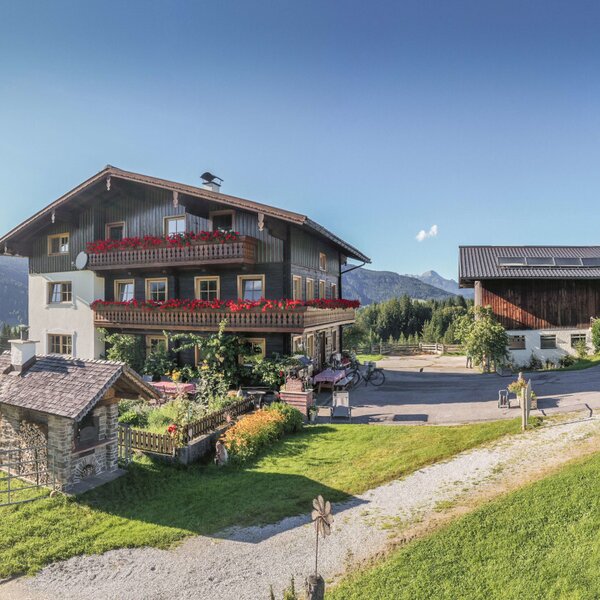 The Farm House complex includes the main building with balconies, a children's playground, and ample parking, surrounded by meadows and mountains.