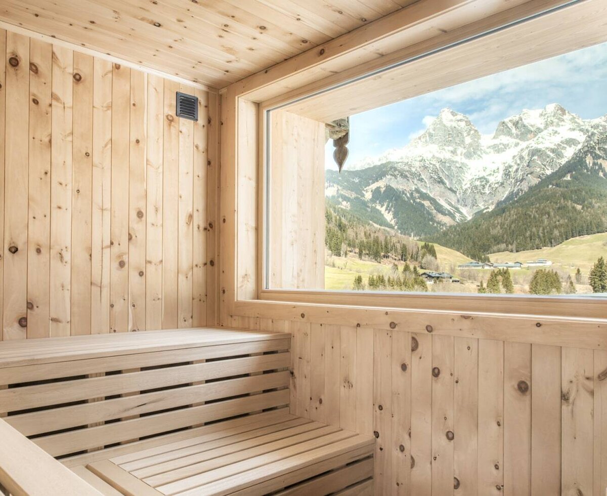 Alm sauna with wooden benches and a large window offering mountain views.