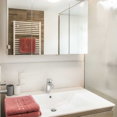 Bathroom in the Alm featuring a sink, wooden vanity cabinet, illuminated mirror cabinet, and a towel warmer.