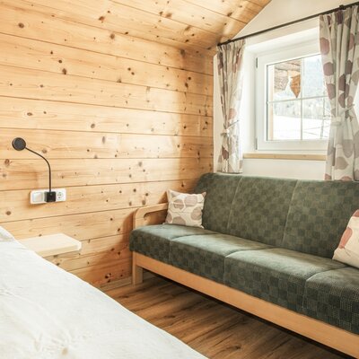 Bedroom in the Alm with wooden walls, a bed, a window, and a green sofa.