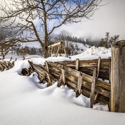 The winter landscape at the Farm House, featuring a traditional wooden fence partially covered in snow.