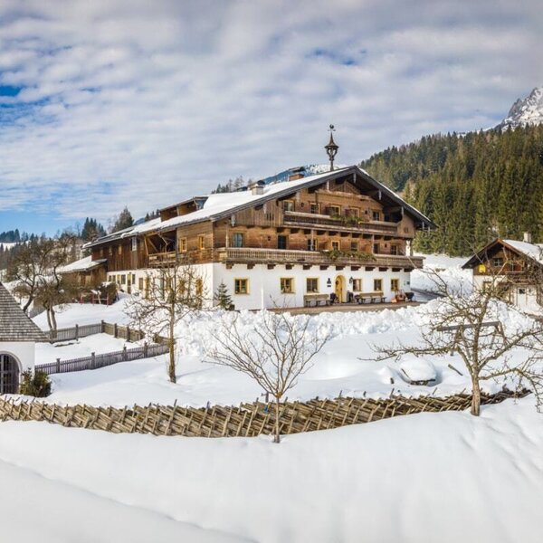 The Erbhof Hinterrain farmhouse with traditional wooden balconies, surrounded by snow in the mountainous winter landscape.