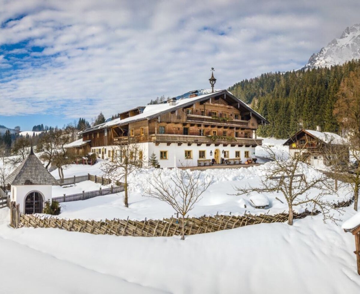 The Erbhof Hinterrain farmhouse with traditional wooden balconies, surrounded by snow in the mountainous winter landscape.