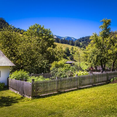 The farm house grounds feature a small white chapel, a fenced garden, and mountain views.