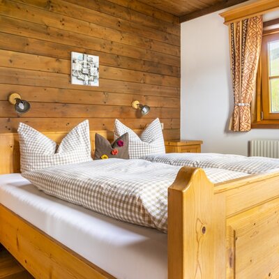 Farm House bedroom featuring wooden paneling, two wooden single beds with checkered bedding, nightstands, and a window overlooking green hills.