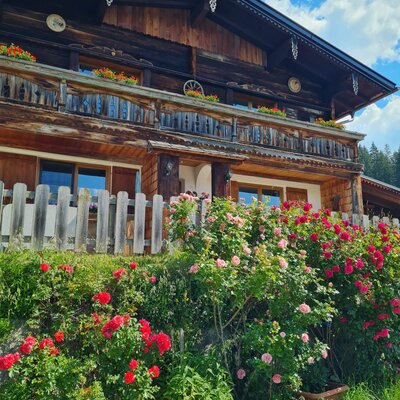 Exterior view of the guesthouse with a traditional wooden facade, a balcony with flower boxes, and a rose garden in the foreground.