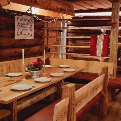 The farmhouse dining area provides a large wooden table with built-in benches, set with plates and candles, amidst rustic wooden walls and traditional decor.