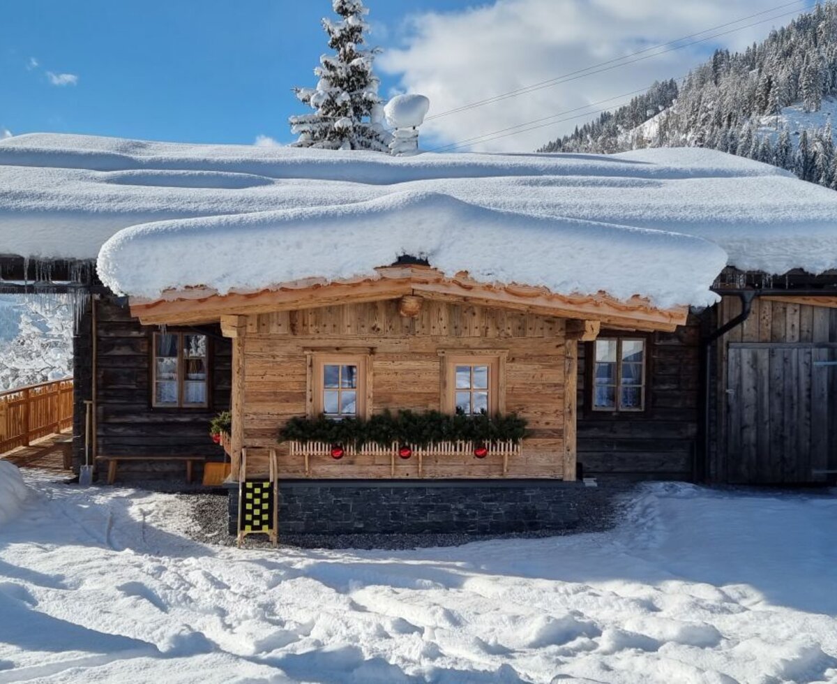 The wooden farmhouse in a snowy mountain setting, featuring decorated window boxes and a covered balcony.