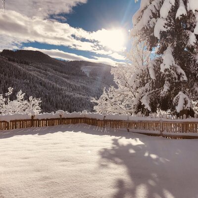 The snowy outdoor area at the farmhouse, featuring a wooden fence, snow-laden trees, and mountain scenery.