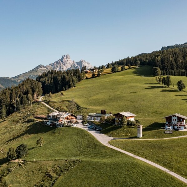 An aerial view of the Farm House complex, set on a green hillside surrounded by forests and distant mountains.