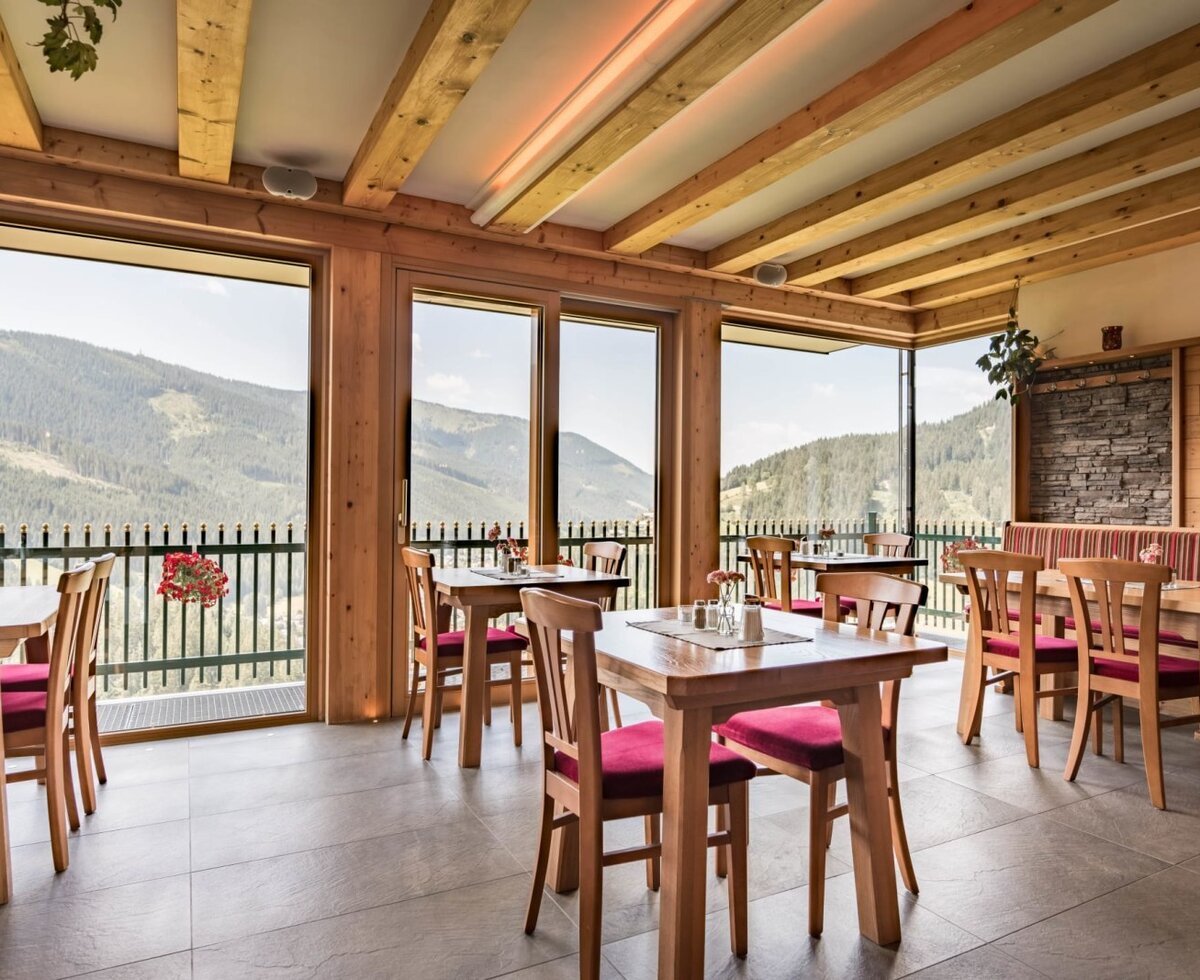 Farmhouse dining area with wooden tables, chairs, and large windows offering unobstructed views of the natural landscape.