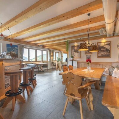 Dining area of the farmhouse featuring wooden tables, benches, a bar, and large windows with views of the natural landscape.