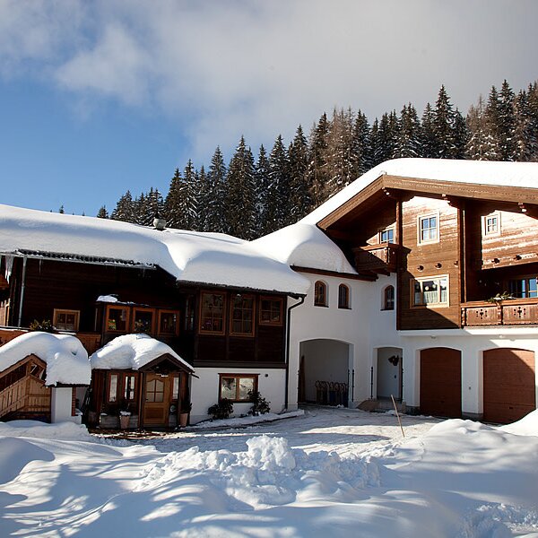 The exterior of the Farm House, featuring snow-covered roofs, balconies, and a backdrop of pine trees.