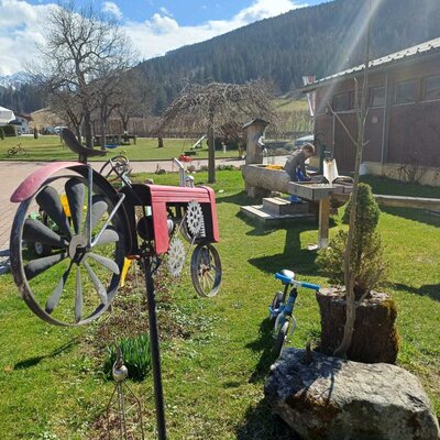 The farmhouse garden with a child playing at the water trough, a decorative tractor, and mountain views.