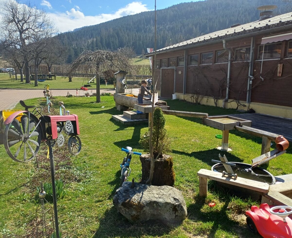 The outdoor area of the farmhouse, featuring a water play structure, sandpit, and play equipment.