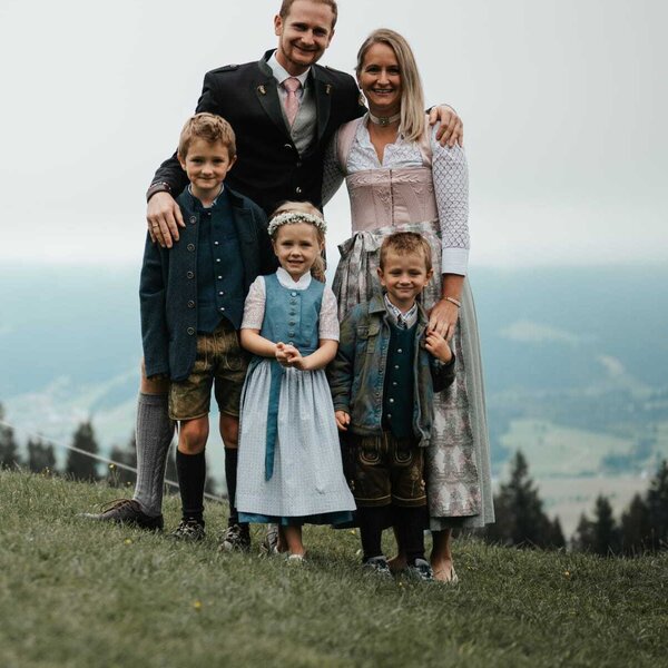 The host family of the farmhouse in traditional attire with a mountain backdrop.