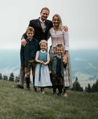 The host family of the farmhouse in traditional attire with a mountain backdrop.