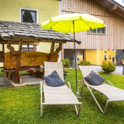 An inviting garden area at the farmhouse featuring comfortable sun loungers, a bright parasol, and a rustic covered wooden seating bench.
