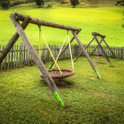 The farmhouse's inviting playground with wooden swings set against a backdrop of lush green meadows.
