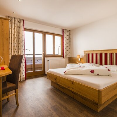 Double bedroom at the holiday farm with a wooden bed frame, wardrobe, a desk area, TV, and direct access to a balcony.
