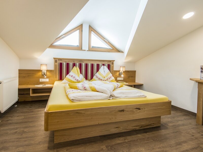 Double bedroom in the farmhouse featuring a wooden bed, two triangular skylights in the slanted ceiling, and a desk with a chair.