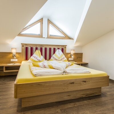 Double bedroom in the farmhouse featuring a wooden bed, two triangular skylights in the slanted ceiling, and a desk with a chair.