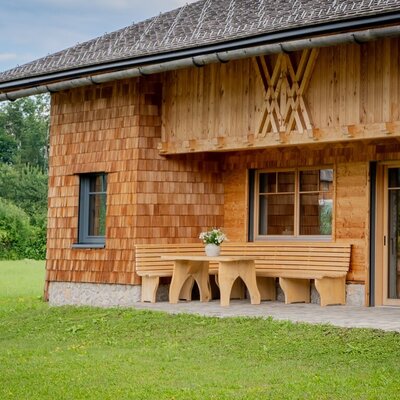The Farm House exterior features wooden shingle and plank siding, a paved terrace with a wooden table and benches, and a surrounding lawn.