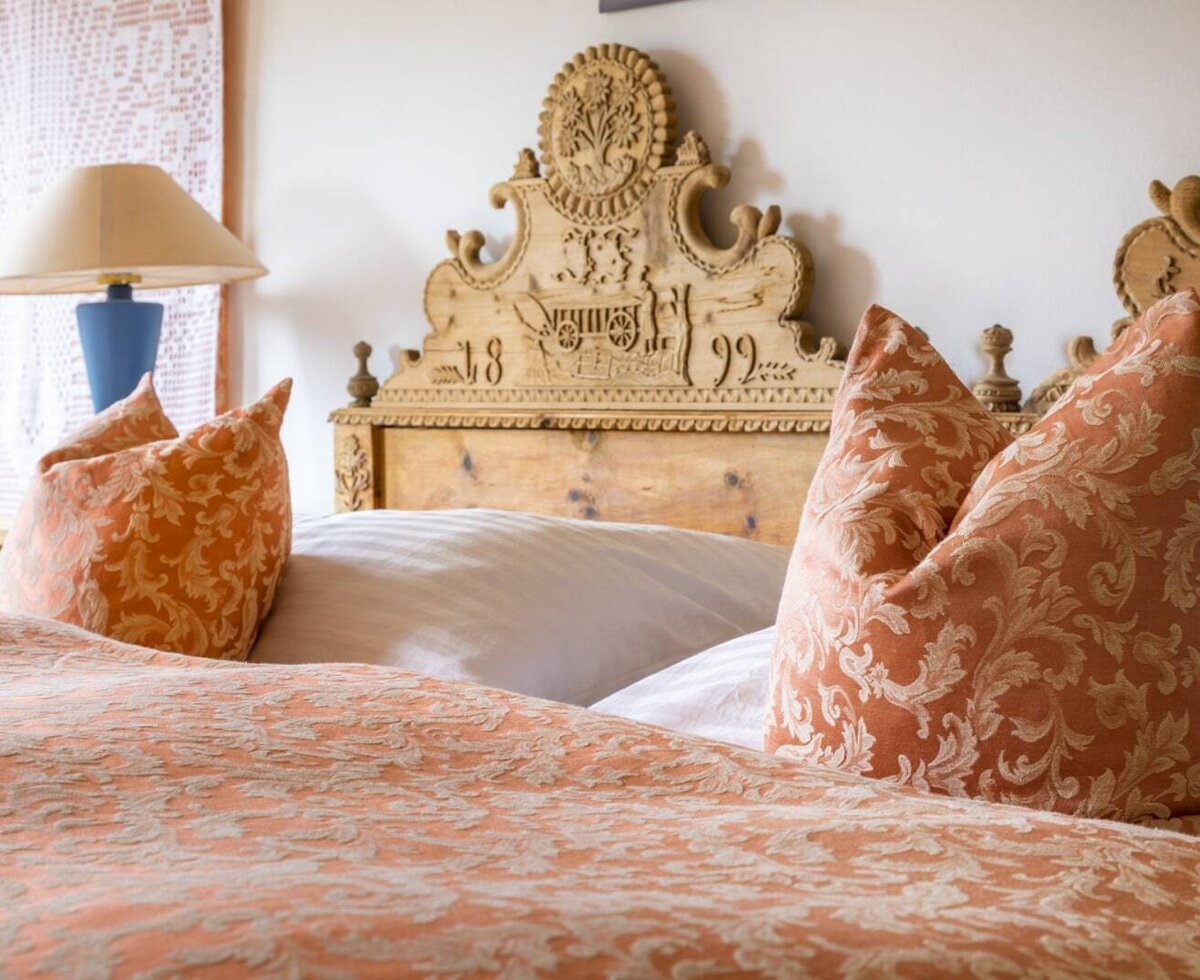 Bedroom in the vacation rental featuring a carved wooden headboard, patterned orange bedding, and a bedside lamp.
