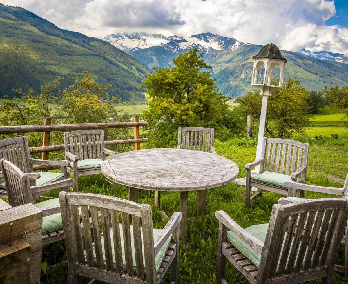 Outdoor dining area at the vacation rental with a wooden table, cushioned chairs, and panoramic views of the green valley and snow-capped mountains.