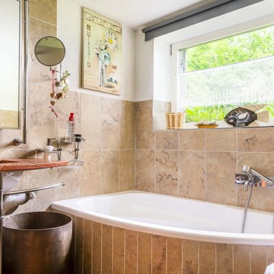 The bathroom in the vacation rental features a bathtub with a shower mixer, a vanity with a sink and mirror cabinet, and a window providing natural light.
