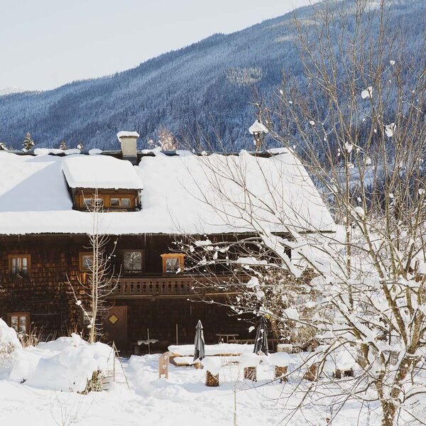 The holiday home in winter, with a snow-covered roof, wooden balcony, and an outdoor seating area.